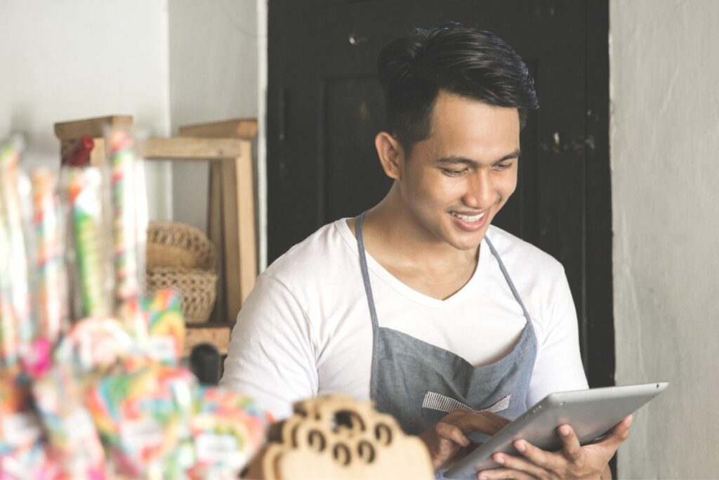 a malaysian businessman smiling because he's managing his business using his ipad