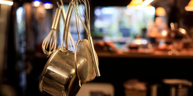 A bunch of kitchen equipment such as pans, a strainer, and whisks