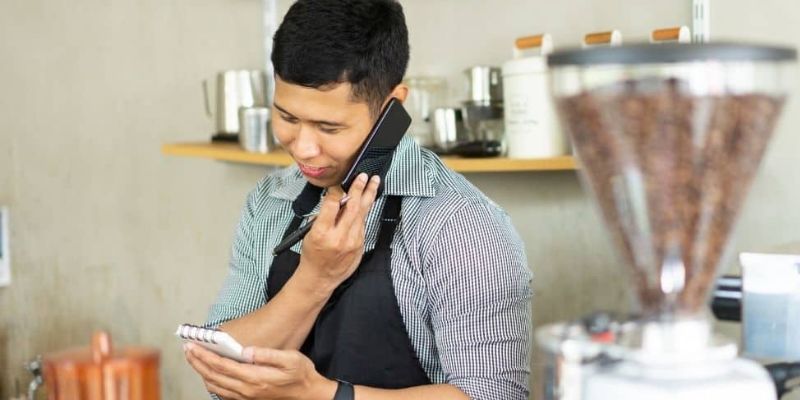 Waiter in a restaurant is on the phone while looking at his notes