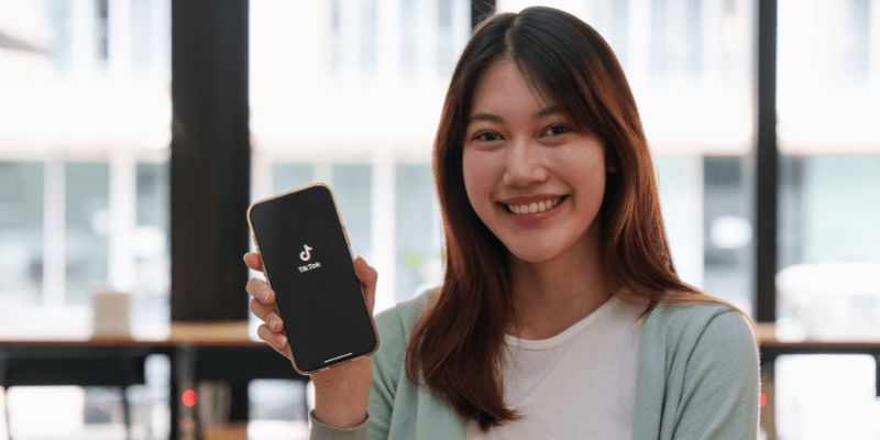 Seorang perempuan sedang menunjukkan aplikasi TikTok melalu telefon pintar.