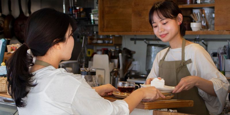 A barista handing over a drink to the waitress