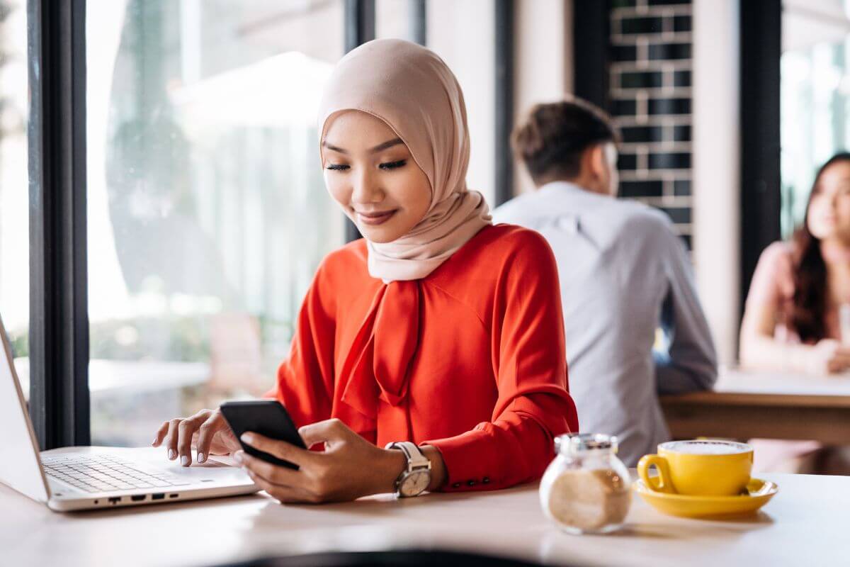 Malaysian business owner looking at her phone and laptop