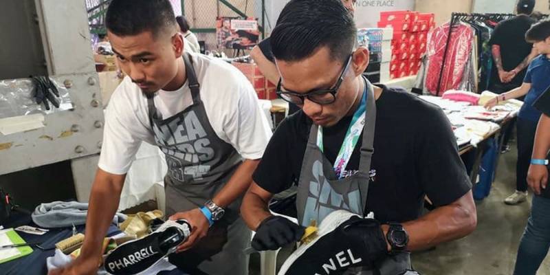 Azrul, co-owner Sneakers Spa sedang membersihkan kasut pelanggan yang berwarna hitam bersama pembantunya.