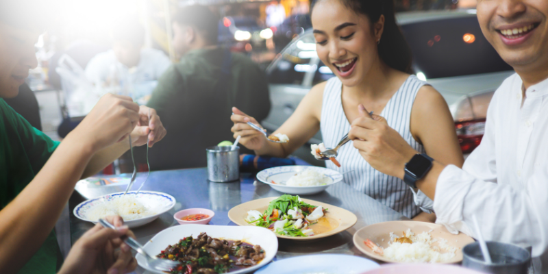 Sekumpulan pelanggan gembira tersenyum sambil menikmati makanan di restoran.
