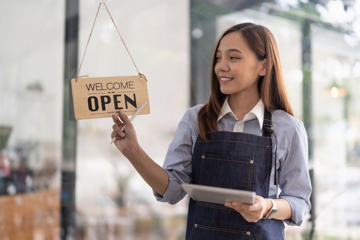 A Filipino cafe owner holding an OPEN sign