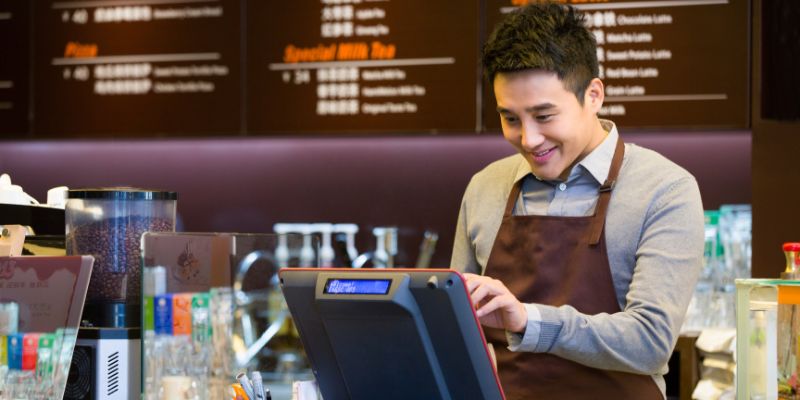 A man cashier is standing in front of the POS system while keying in the order.