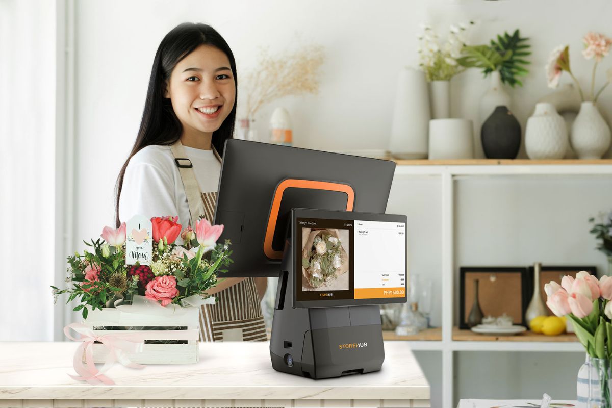 A female cashier is inputting the customer's order into the StoreHub POS system, while the POS displays the total amount in pesos on the screen.