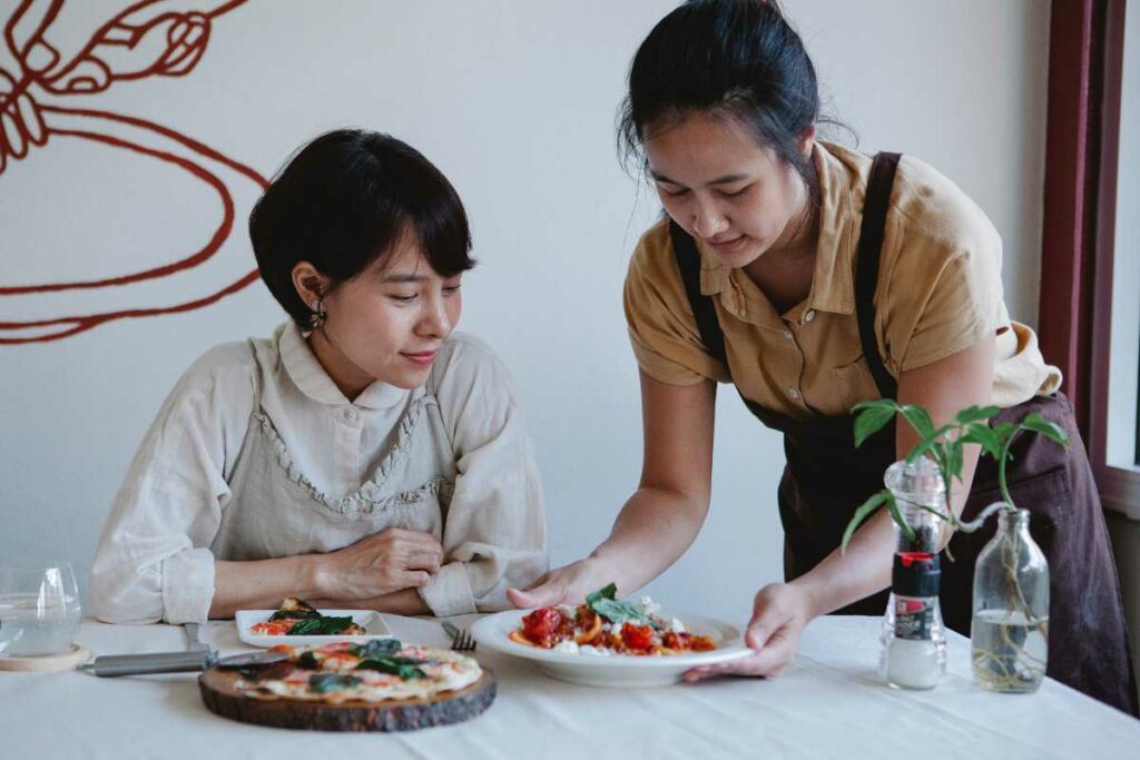 A waitress is serving a plate of pasta to a dine-in customer.