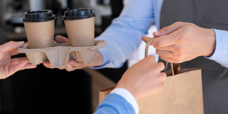 Cafe owner handing over takeaway coffee and a takeaway bag to customer.