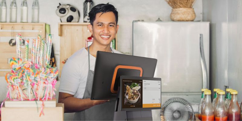 A male restaurant cashier is standing in front of the POS system and ready to check out a customer's order.