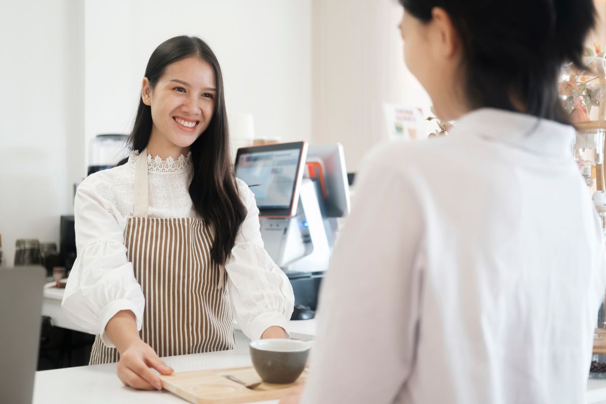 A waitress at a restaurant is smiling at the customer while giving her order.