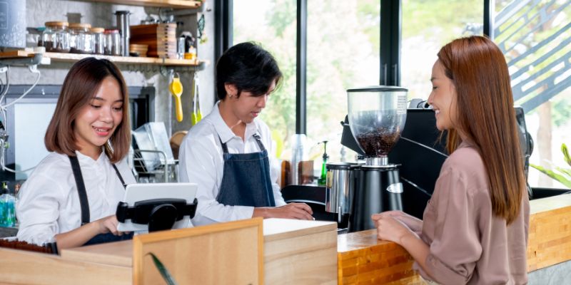 The waitress receives the order from the customer, a woman, while her co-worker is preparing the order. 