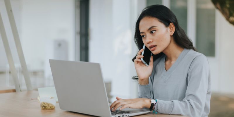 A Filipino woman talking to someone on the phone while typing on her laptop