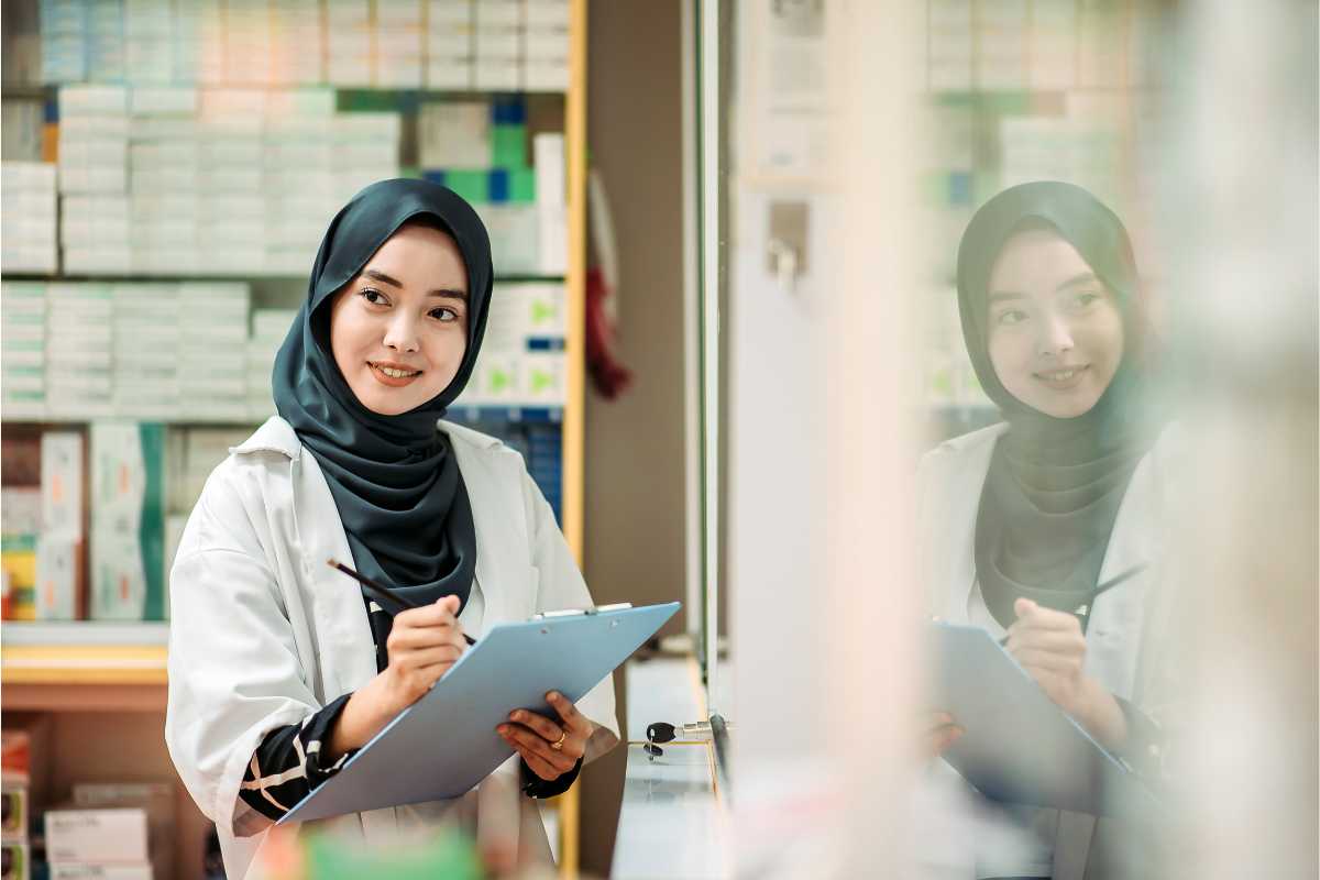 Seorang wanita bertudung sedang memegang pen dan kertas untuk menyemak stok inventori.