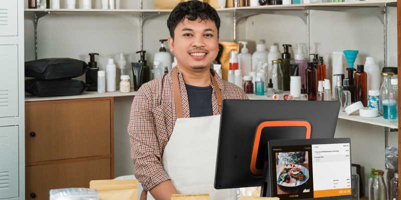 Seorang juruwang lelaki sedang tersenyum sambil menunggu untuk mengambil pesanan pelanggan.