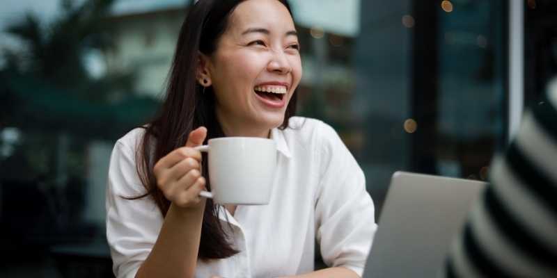 Asian girl laughing while holding a coffee cup in hand in a cafe