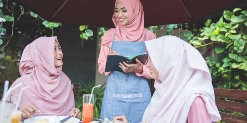 Two Asian ladies talking happily with a staff member in a restaurant.