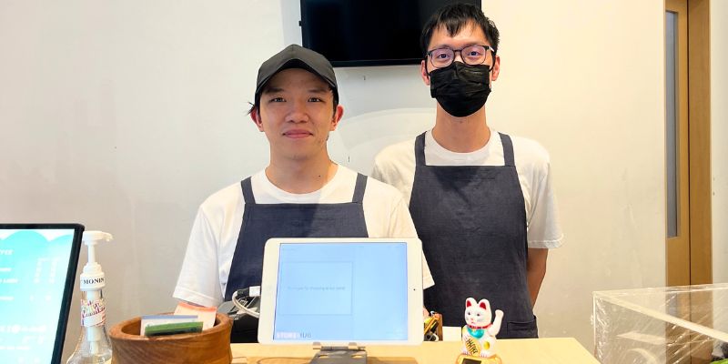 Dua orang peniaga F&B yang memakai apron kelabu sedang berdiri di hadapan sistem POS StoreHub.